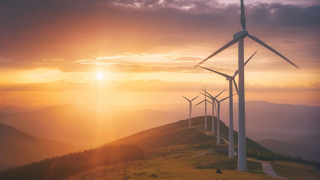 Several wind turbines are silhouetted against a vibrant sunset sky with hues of orange, purple, and blue