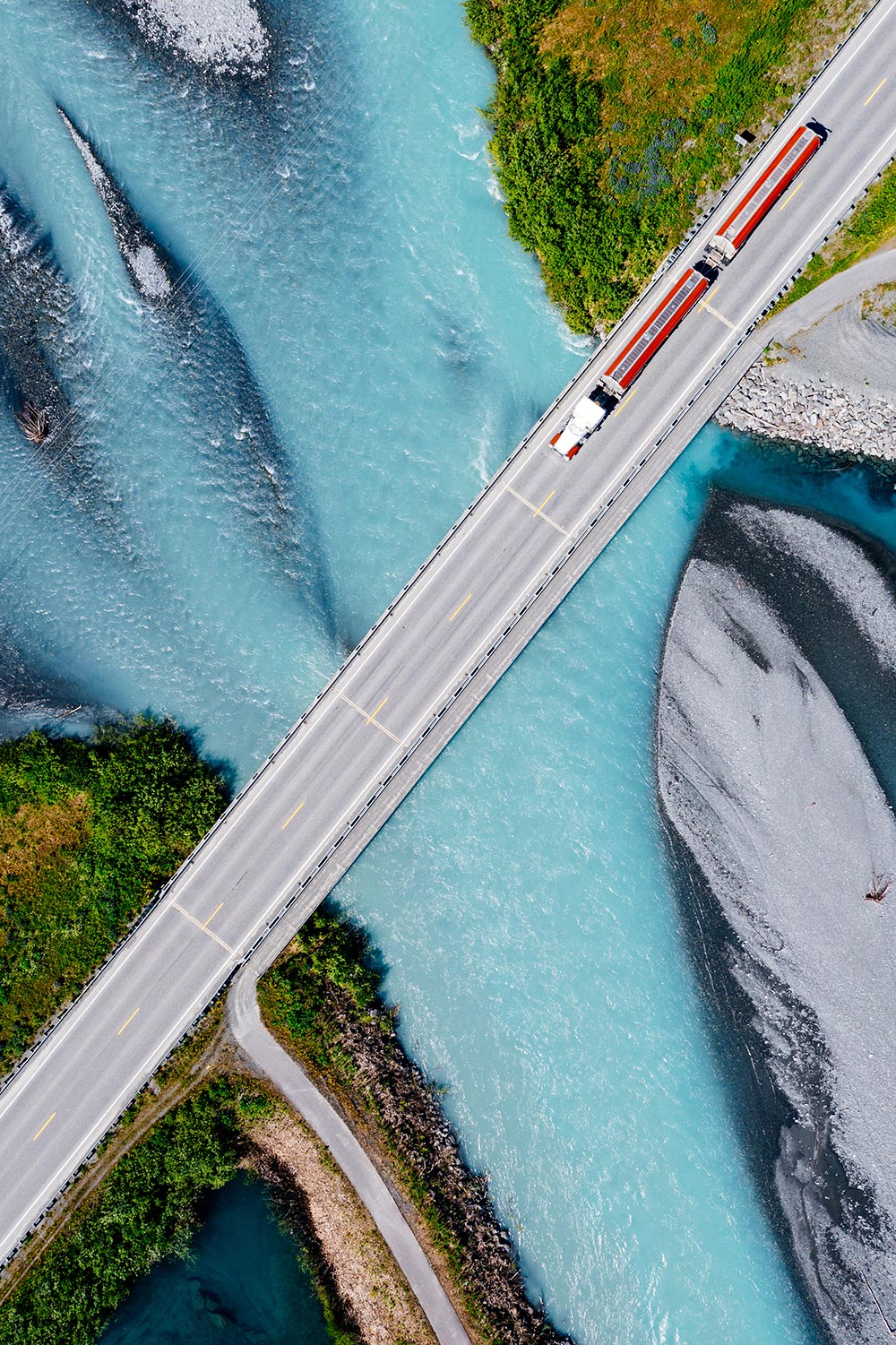 Aerial view of a truck or train crossing a bridge over a turquoise river, illustrating infrastructure and connectivity in environmental research regions